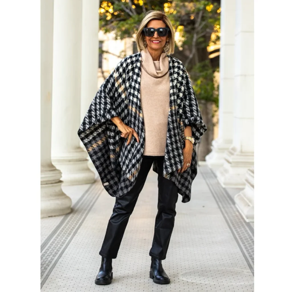 Woman in a houndstooth wrap over a camel cowl-neck sweater with black pants and ankle boots, a polished fall outfit.