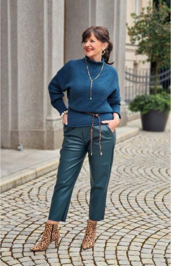 Woman in a teal mock-neck sweater, teal leather-look cropped pants, leopard ankle boots, and a long gold necklace on a cobblestone street