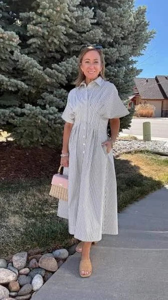 Smiling woman in a striped midi shirt dress holding a small pink and woven basket bag, with tan slide sandals.