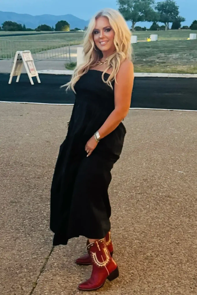 Woman with long blonde waves in a black strapless smocked dress, red cowboy boots, and a chunky gold chain necklace.