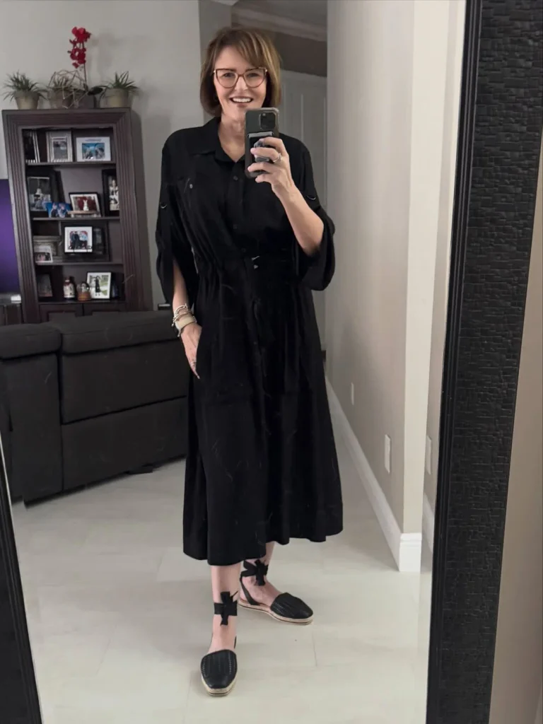 Woman in glasses wearing a black midi shirt dress with a drawstring waist and black lace-up espadrilles.